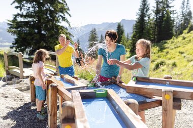 Vater und Mutter, die gemeinsam mit ihren zwei Töchtern beim Wasserspiel auf Golmis Forschungspfad die Kraft des Wassers entdecken | © Golm Silvretta Lünersee Tourismus GmbH Bregenz, Stefan Kothner